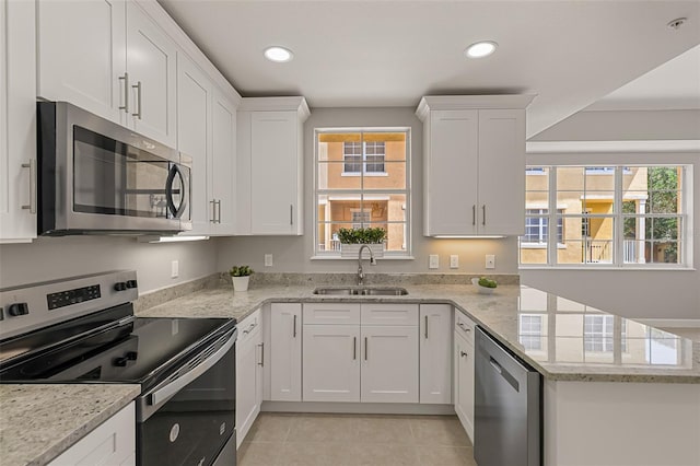 kitchen featuring stainless steel appliances, a sink, white cabinetry, a peninsula, and light stone countertops