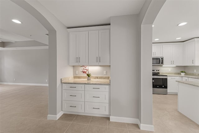kitchen with appliances with stainless steel finishes, arched walkways, light tile patterned floors, and recessed lighting
