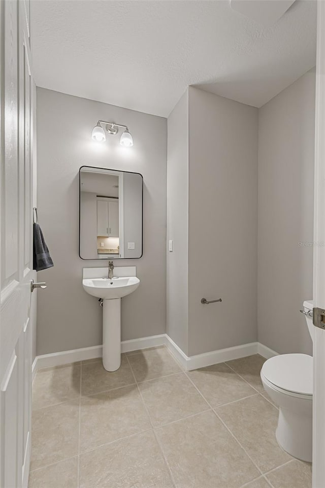 bathroom with tile patterned flooring, toilet, baseboards, and a textured ceiling