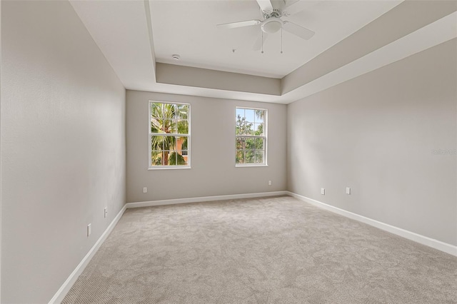 carpeted spare room with baseboards, a ceiling fan, and a tray ceiling