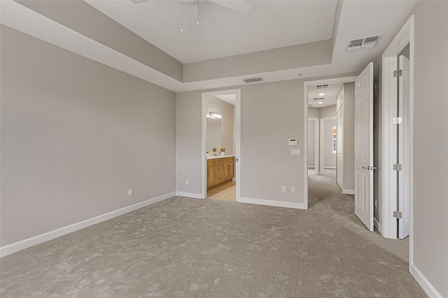 unfurnished bedroom featuring light carpet, baseboards, ensuite bath, and a tray ceiling