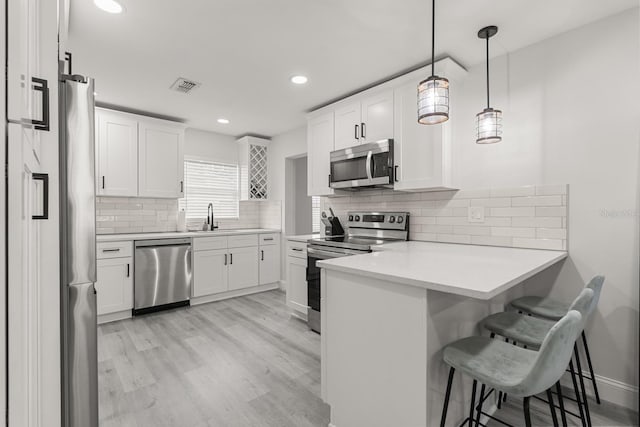 kitchen featuring a peninsula, a breakfast bar, a sink, light wood-style flooring, and appliances with stainless steel finishes