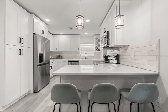 kitchen featuring light wood-type flooring, light countertops, white cabinets, a peninsula, and stainless steel appliances