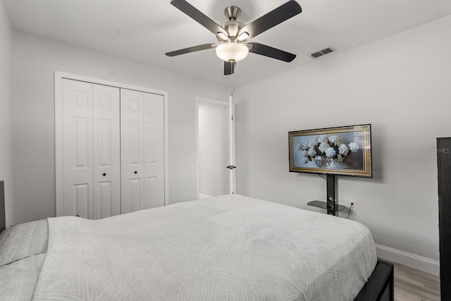 bedroom featuring ceiling fan, visible vents, wood finished floors, baseboards, and a closet