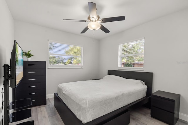 bedroom with a ceiling fan, baseboards, multiple windows, and light wood finished floors