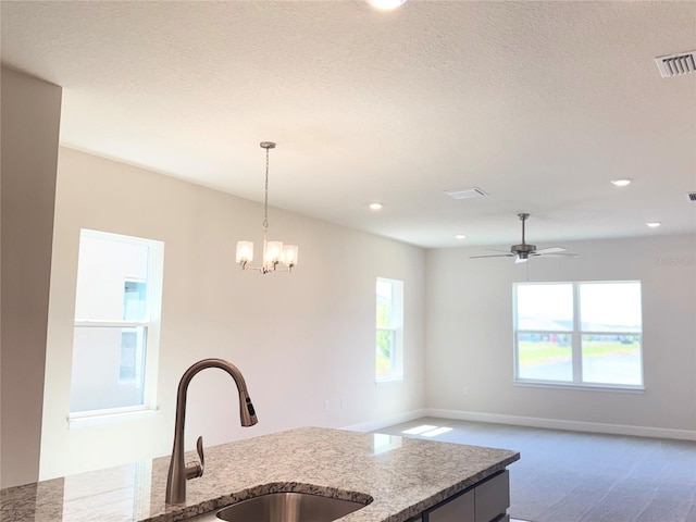 kitchen with visible vents, a healthy amount of sunlight, light stone counters, a sink, and hanging light fixtures