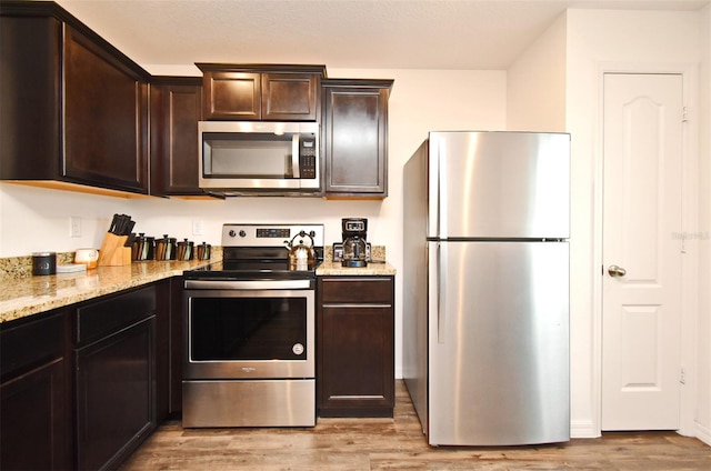 35734 Rose Moss Ave, Leesburg, FL 34788 - kitchen with dark brown cabinetry, appliances with stainless steel finishes, light stone counters, and light wood-type flooring