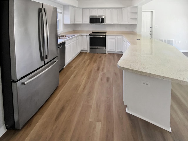kitchen with visible vents, light wood-type flooring, a sink, a peninsula, and stainless steel appliances