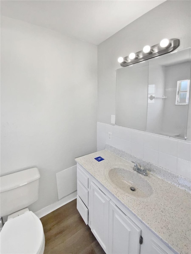 bathroom with vanity, decorative backsplash, wood finished floors, toilet, and baseboards