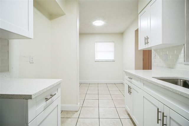 kitchen featuring light tile patterned flooring, light stone countertops, baseboards, white cabinetry, and a sink