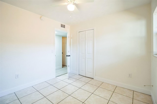 unfurnished bedroom featuring visible vents, a closet, baseboards, a ceiling fan, and light tile patterned floors
