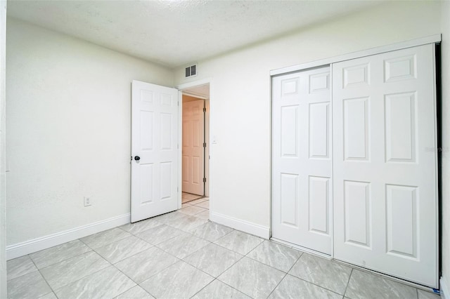 unfurnished bedroom with baseboards, visible vents, light tile patterned floors, and a closet