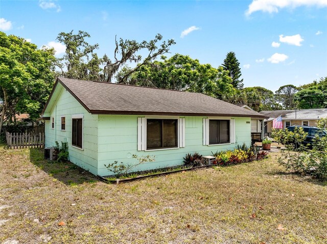 view of front facade with roof with shingles, fence, central AC, and a front yard