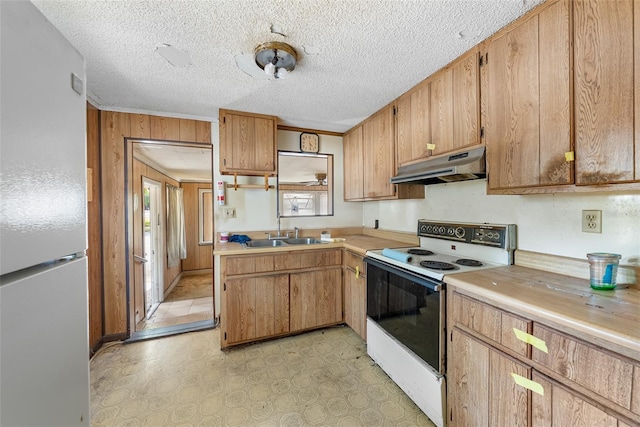 kitchen featuring a sink, light countertops, wooden walls, under cabinet range hood, and white appliances