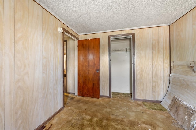unfurnished bedroom featuring wooden walls, a textured ceiling, carpet floors, and a closet