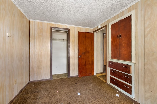 unfurnished bedroom featuring crown molding, wooden walls, carpet floors, and a closet