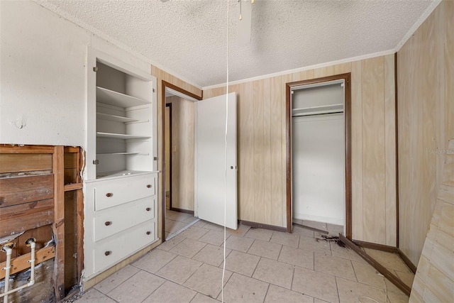 unfurnished bedroom with a closet, a textured ceiling, light tile patterned flooring, and wooden walls