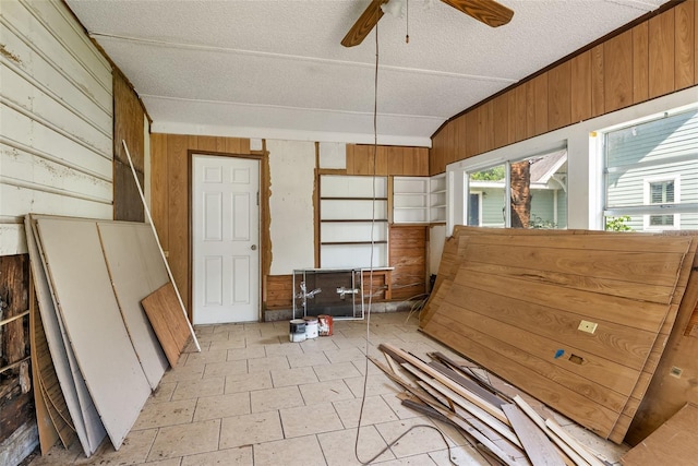 misc room with a ceiling fan, a textured ceiling, and wood walls
