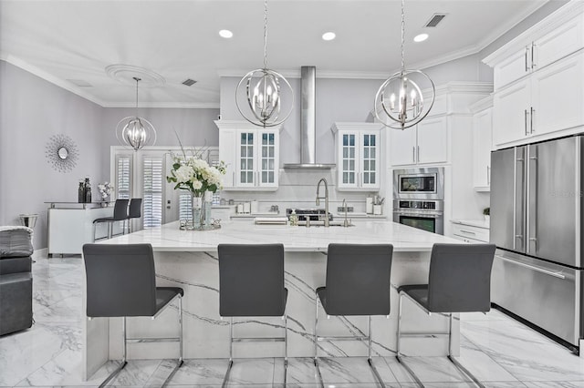 1450 Belfiore Way, Windermere, FL 34786 - kitchen with stainless steel appliances, a chandelier, white cabinets, wall chimney range hood, and light marble finish floors