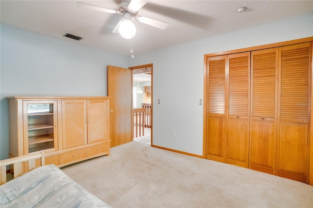 unfurnished bedroom featuring a ceiling fan, a textured ceiling, light colored carpet, visible vents, and a closet
