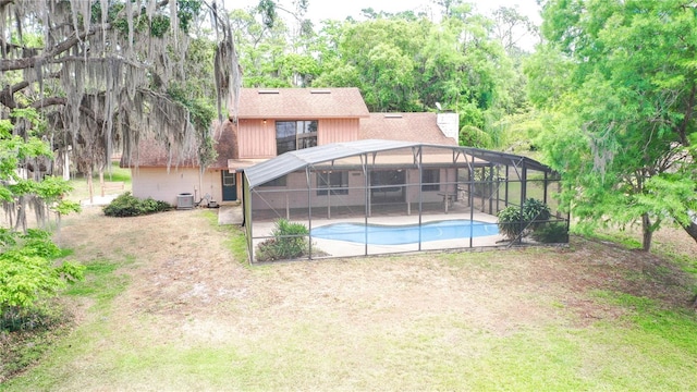 back of property with glass enclosure, a shingled roof, a patio area, and an outdoor pool