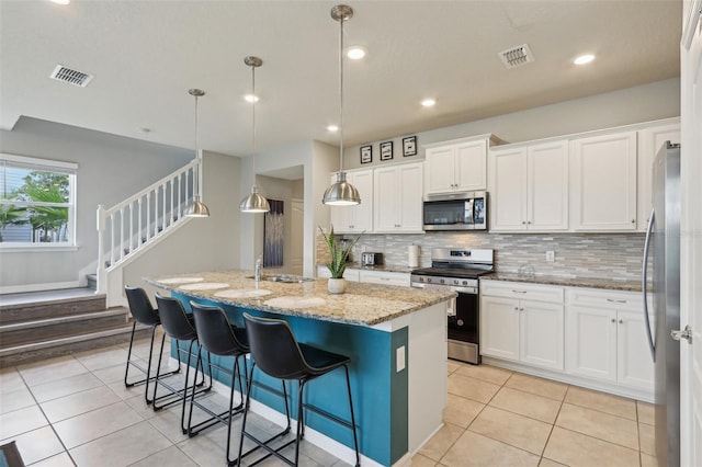 7554 Oak Spring Ln, Davenport, FL 33837 - kitchen featuring appliances with stainless steel finishes, light tile patterned floors, white cabinets, a center island with sink, and decorative backsplash
