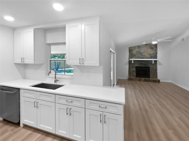 kitchen with stainless steel dishwasher, light countertops, white cabinetry, a sink, and light wood-style flooring