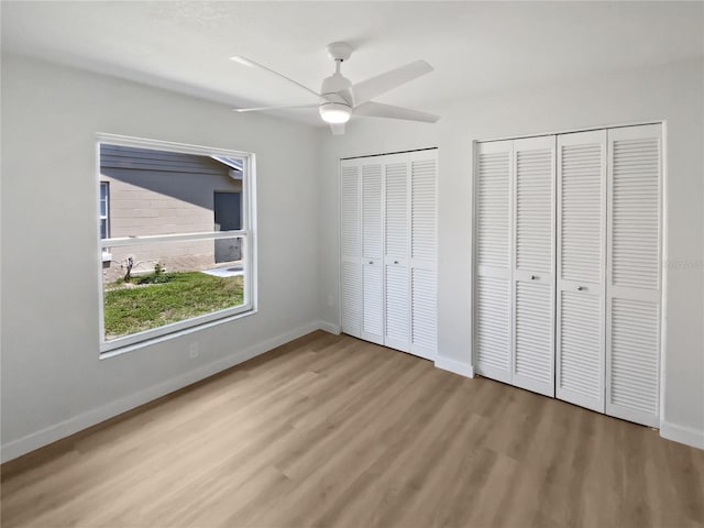 unfurnished bedroom featuring two closets, a ceiling fan, baseboards, and wood finished floors
