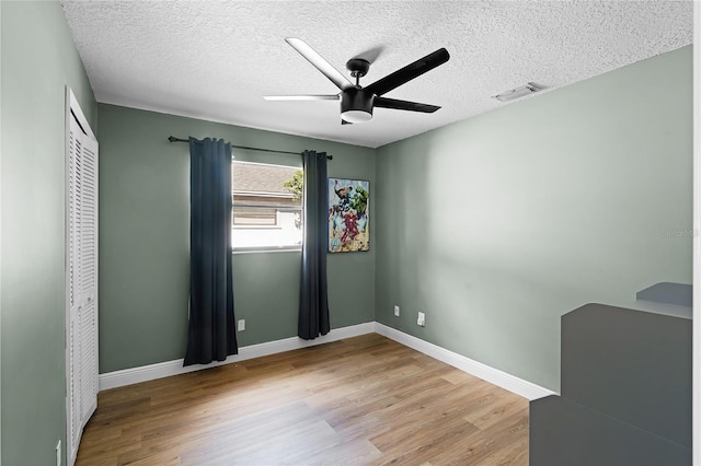 empty room featuring a ceiling fan, a textured ceiling, visible vents, wood finished floors, and baseboards