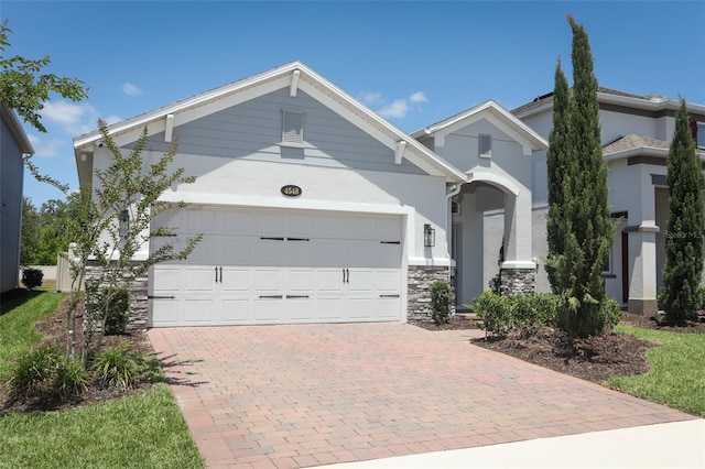 view of front of home featuring a garage, stucco siding, decorative driveway, and stone siding