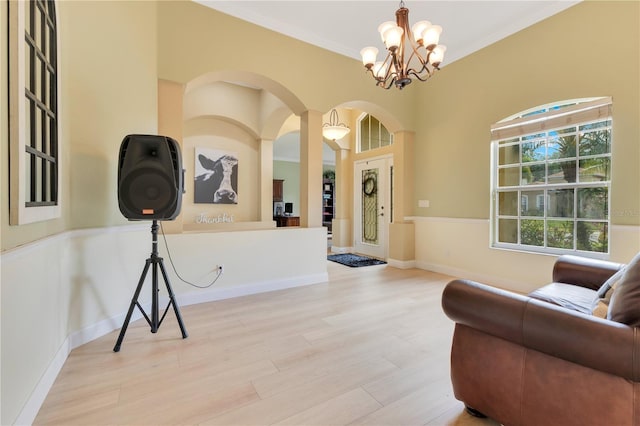 living area with crown molding, arched walkways, a chandelier, and light wood-type flooring