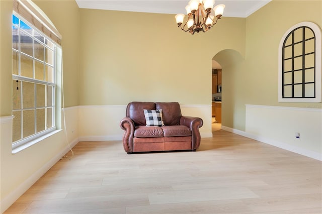 living area with a healthy amount of sunlight, arched walkways, an inviting chandelier, and light wood-type flooring