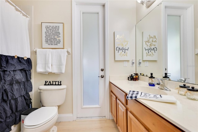 bathroom featuring vanity, toilet, a shower with shower curtain, baseboards, and wood finished floors