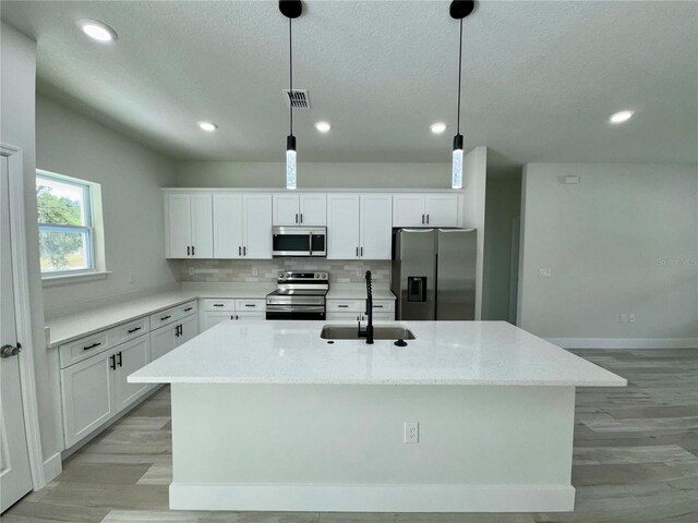 kitchen with a kitchen island with sink, light wood-type flooring, white cabinetry, a sink, and stainless steel appliances