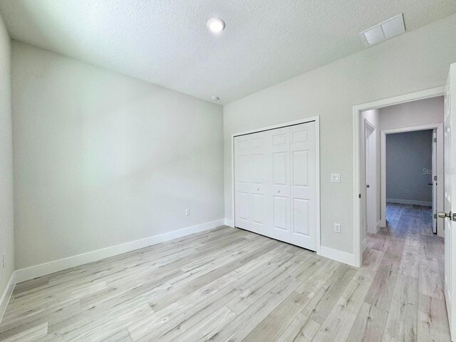 unfurnished bedroom featuring baseboards, light wood-style flooring, a textured ceiling, and visible vents
