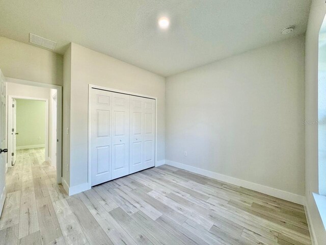 unfurnished bedroom featuring baseboards, light wood finished floors, visible vents, and a closet