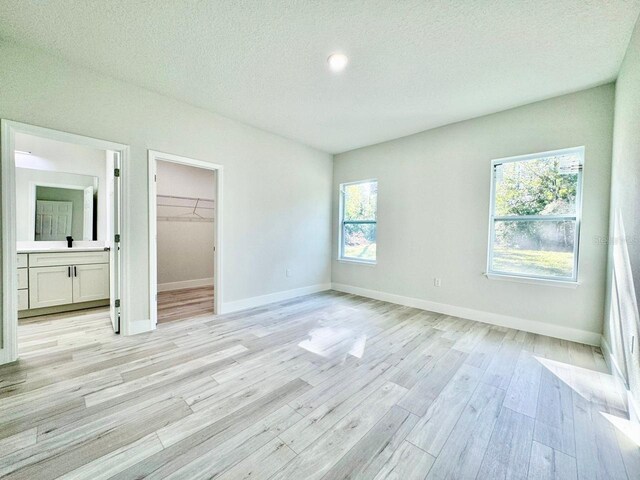 unfurnished bedroom with baseboards, a textured ceiling, a walk in closet, and light wood-type flooring