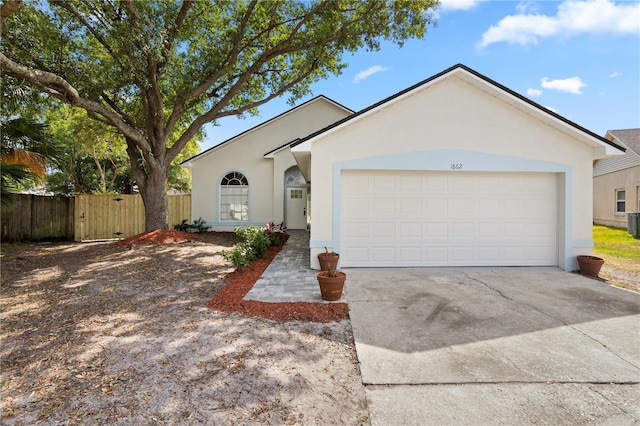 ranch-style home with a garage, fence, stucco siding, and driveway