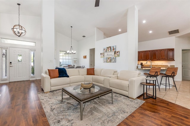 living room featuring high vaulted ceiling, visible vents, wood finished floors, and a notable chandelier