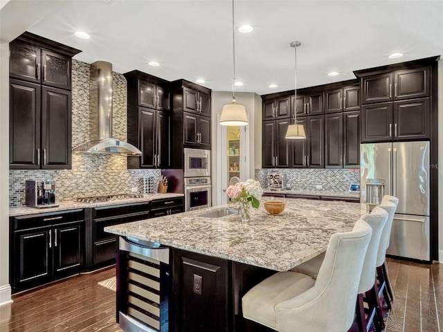 kitchen with wall chimney range hood, light stone counters, a sink, stainless steel appliances, and dark wood-style floors