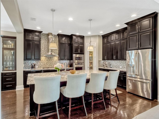 kitchen featuring wall chimney range hood, stainless steel appliances, decorative backsplash, and dark wood-type flooring