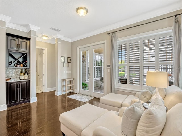 living room featuring visible vents, crown molding, baseboards, dark wood-style floors, and ornate columns