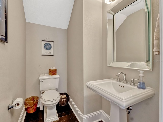 half bath with a sink, toilet, baseboards, wood finished floors, and lofted ceiling