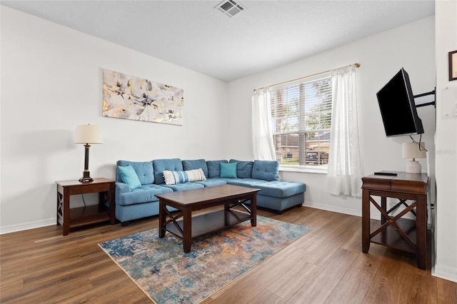 living room with baseboards, visible vents, and wood finished floors