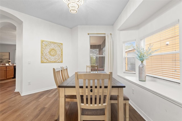 dining space featuring arched walkways, baseboards, and wood finished floors