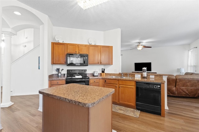 kitchen with light wood finished floors, a sink, a peninsula, open floor plan, and black appliances