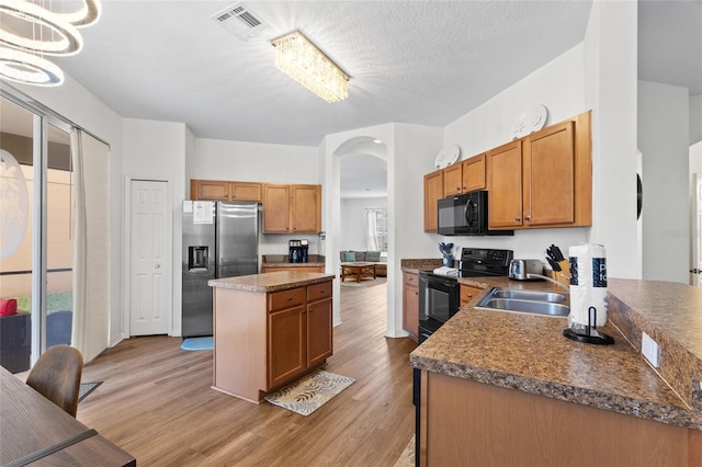 kitchen featuring light wood-style flooring, a sink, black appliances, arched walkways, and a kitchen island