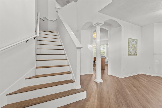 stairway with arched walkways, baseboards, decorative columns, and wood finished floors
