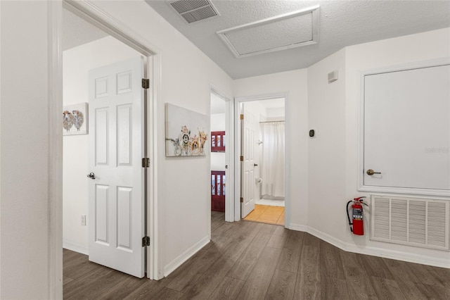 hallway with attic access, visible vents, baseboards, and dark wood-style floors