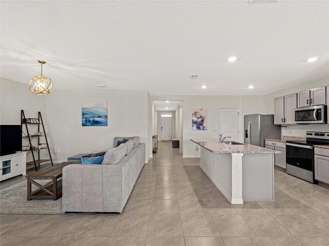 kitchen featuring gray cabinets, appliances with stainless steel finishes, a center island with sink, a sink, and light stone counters